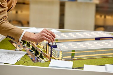 Kağıt üzerinde planı olan erkek mimar, kırtasiye ve 3D yapı modeli ofiste çalışıyor.