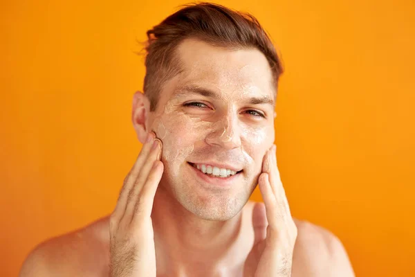 Hombre caucásico joven aplicar crema hidratante para la cara para una piel brillante saludable, aislado — Foto de Stock