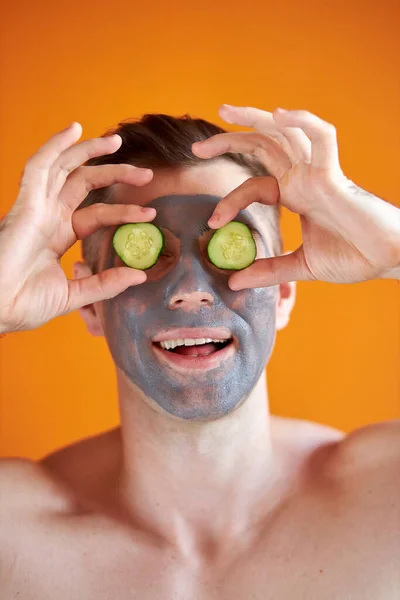 Retrato de alegre caucásico hombre witn belleza facial máscara y pepino — Foto de Stock