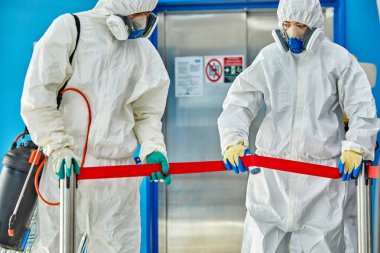 Virüs korumalı giysiler giyen ve binaları dezenfekte eden adamlar.