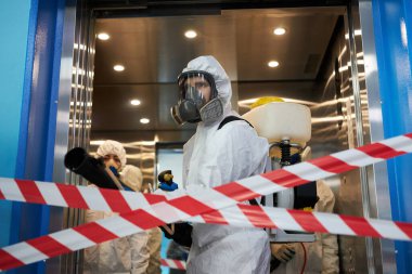 Tehlikeli madde giysileri içindeki işçiler kapalı alanda dezenfeksiyon yaparken maske takıyorlar.