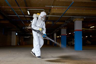 Tehlikeli madde giysisi içindeki genç temizlik işçisi basınç temizleyicisi ya da dezenfektanla çalışıyor.