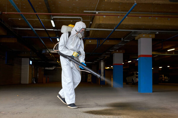 young sanitation worker in hazmat suit working with pressure washer or sanitizer