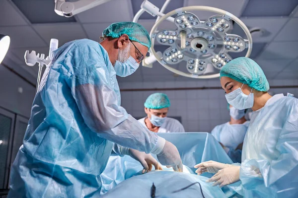 Équipe amicale de chirurgiens caucasiens en salle d'opération avec équipement chirurgical — Photo