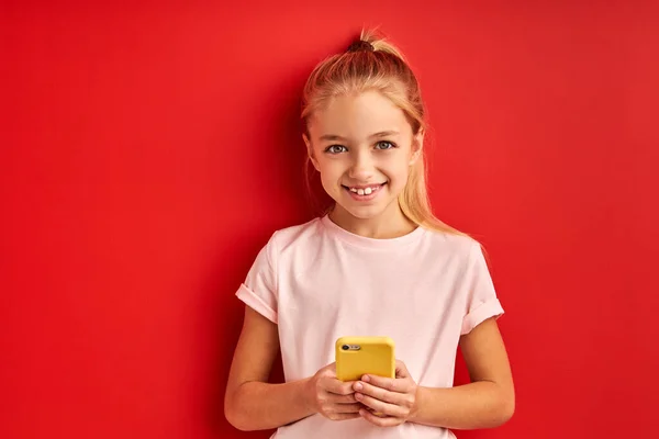Blond kind meisje gebruik smartphone, geïsoleerd op rode achtergrond — Stockfoto
