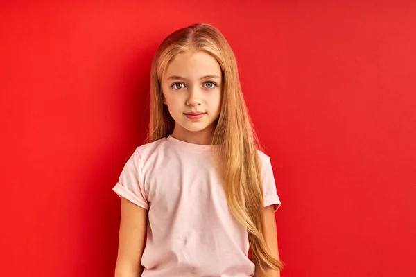 Сором'язлива впевнена біла дівчинка ізольована на червоному студійному фоні — стокове фото