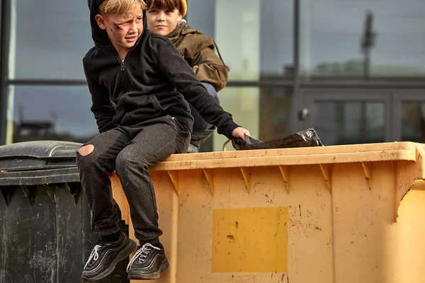 Kaukasiska utstötta barn går på stadens gator, sitter på en soptunna — Stockfoto