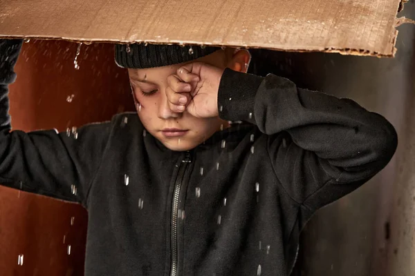 貧しい孤児の少年は段ボールの下の雨から避難し — ストック写真