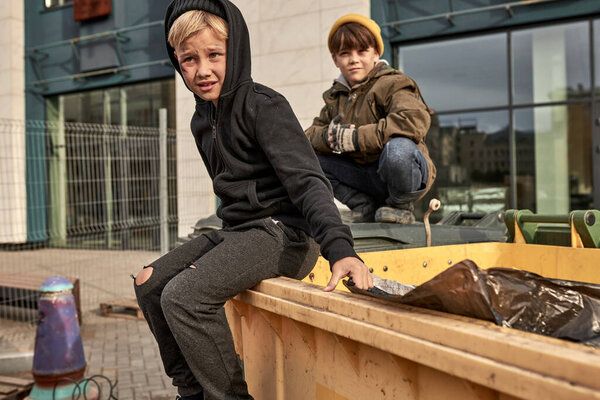 two homeless orphans sit on public trash can