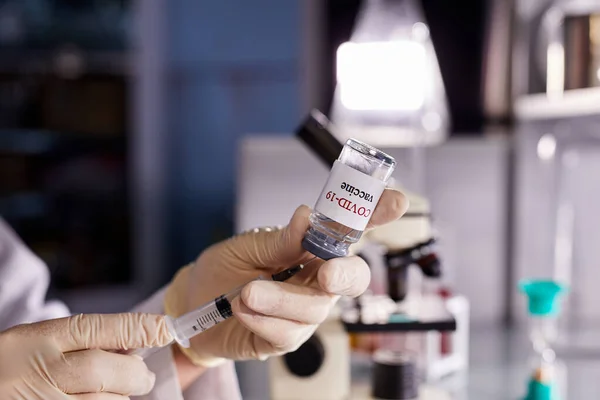scientist takes medicine with a vaccine from an ampoule with a syringe with the text COVID -19