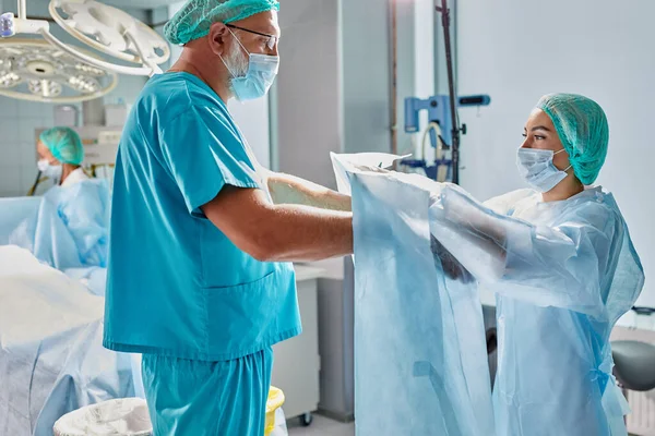 Équipe de médecins proches aider à porter l'uniforme médical les uns aux autres, préparer — Photo