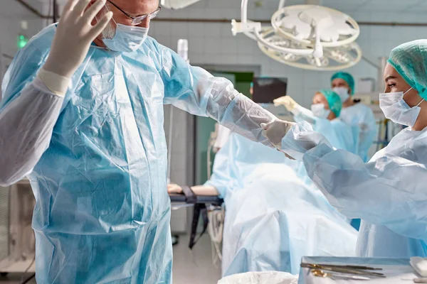 Médico assistente amigável ajuda cirurgião sênior a usar uniforme — Fotografia de Stock