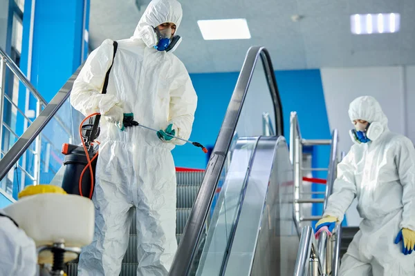 Desinfectoren in virusbeschermende pakken en masker desinfecterende gebouwen van het coronavirus met het spuitapparaat — Stockfoto