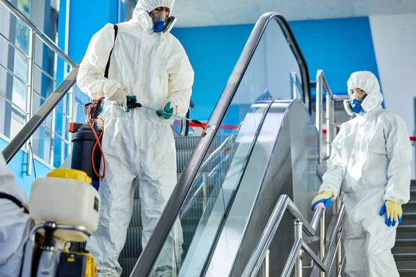 Equipe de corajosos desinfetantes esterilizando a escada rolante e shopping center building — Fotografia de Stock