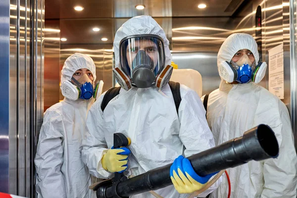 Απολυμαντικά με προστατευτικές στολές ιών και απολυμαντικά μασκών κτιρίων του κορωναϊού με τον ψεκαστήρα — Φωτογραφία Αρχείου