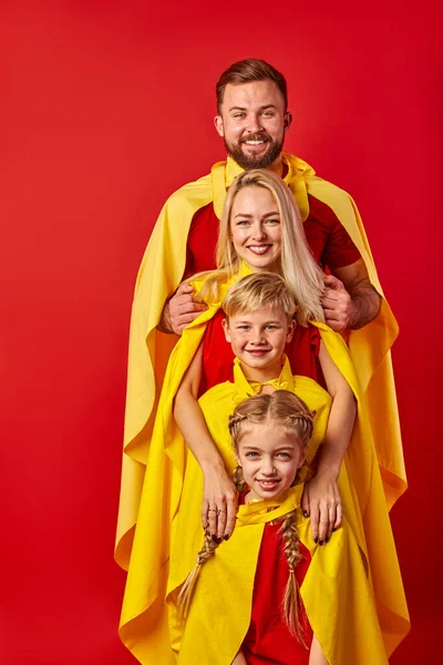 Familie van superhelden in kostuums poseren in studio met rode achtergrond — Stockfoto