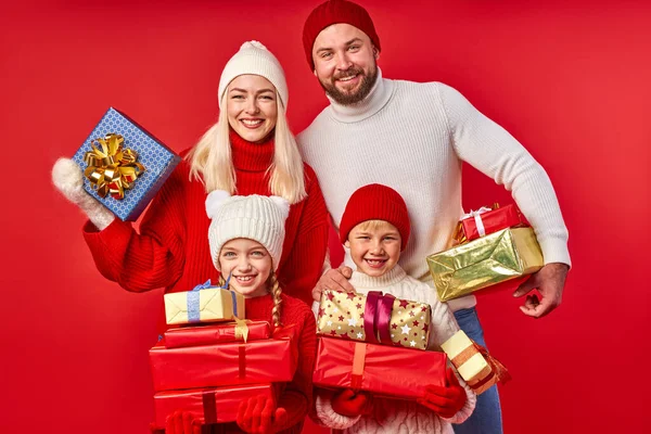 Счастливые родители и дети в зимней одежде держат подарки в руках изолированы на красный — стоковое фото