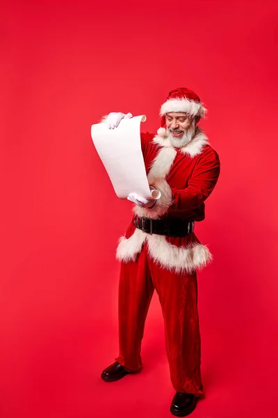 Взволнованный Санта-Клаус в костюме держа пергамент рулон читая письмо список пожеланий — стоковое фото