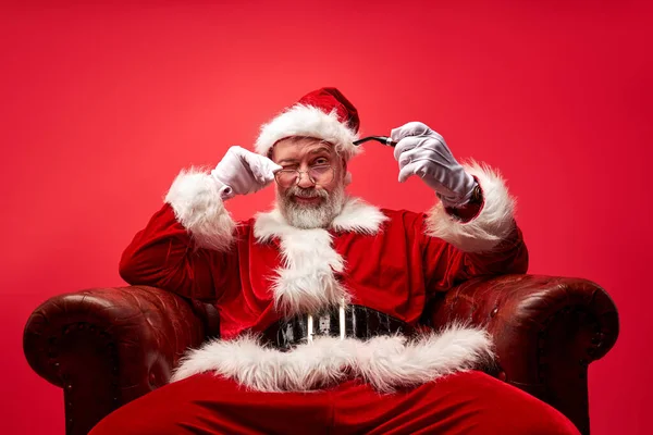 Гордый, высокомерный Санта сидит на стуле изолированы на красном фоне — стоковое фото