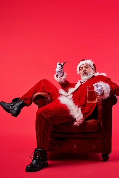 Надменный пожилой Санта Клаус в костюме сидит на стуле — стоковое фото