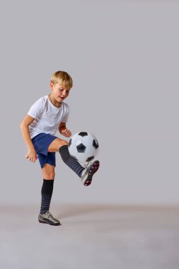 Atletik beyaz çocuk profesyonel olarak stüdyoda futbol topuyla antrenman yapıyor.