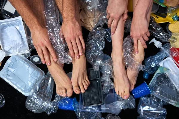 Foto cortada de pernas de casal deitado na sala cheia de sujeira, resíduos de plástico — Fotografia de Stock