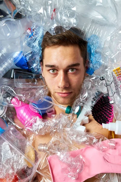 Giovane uomo caucasico sullo sfondo di bottiglie di plastica vuote e rifiuti — Foto Stock