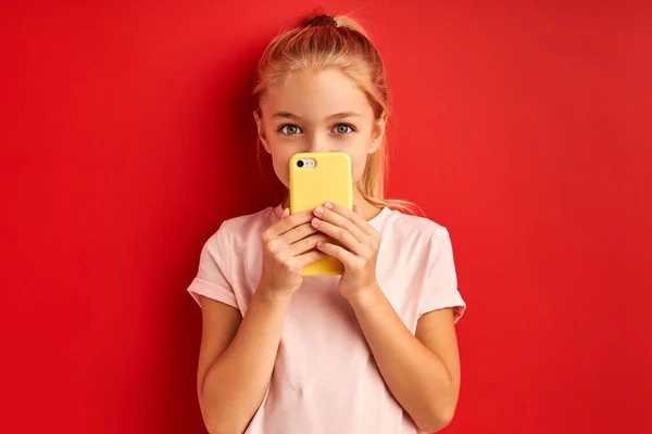 Blond kind meisje gebruik smartphone, geïsoleerd op rode achtergrond — Stockfoto