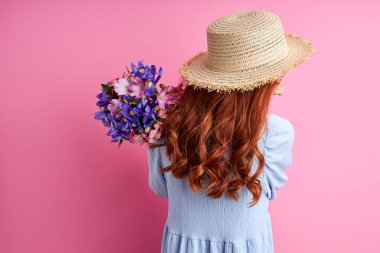 Kızıl saçlı, yaz şapkalı ve çiçekli bir kadın.