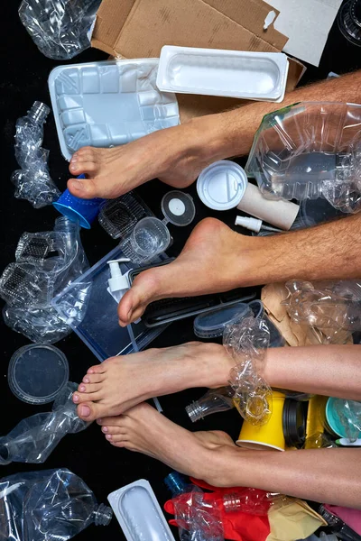 Foto cortada de pernas de casal deitado na sala cheia de sujeira, resíduos de plástico — Fotografia de Stock