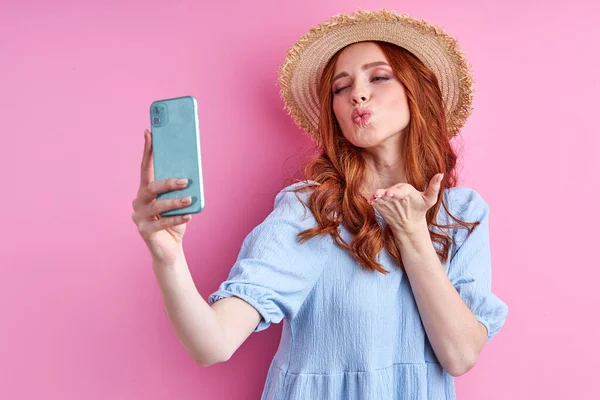 Vrolijke roodharige vrouw blazen een kus op smartphone camera — Stockfoto