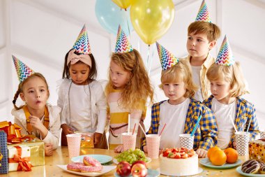 Doğum günü şapkalı neşeli çocuklar doğum gününü kutluyor.