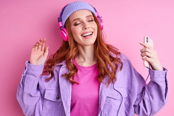 Довольно позитивная рыжая женщина в повседневной одежде слушает музыку — стоковое фото