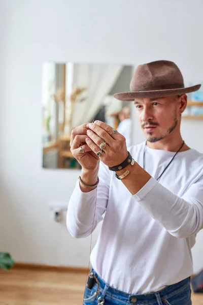 designer male puts thread in a needle for sewing a hat