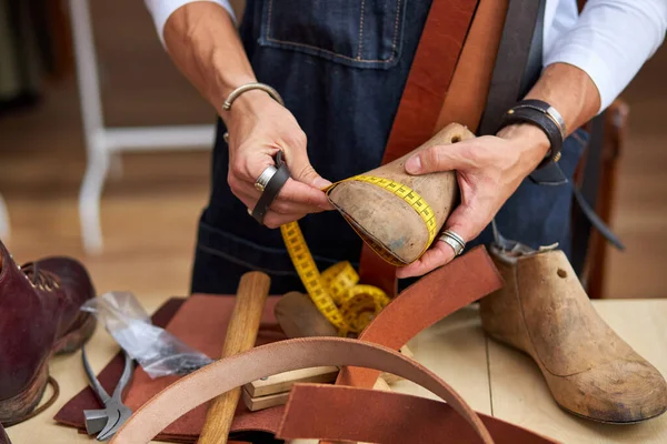 Cordonnier professionnel mesurant une chaussure avec ruban de mesure en atelier — Photo