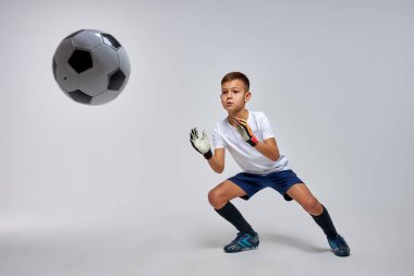 Genç kaleci, gri arka planda izole edilmiş havada futbol topunu yakalıyor.