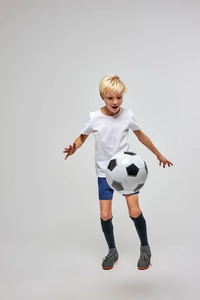 Jovem menino joelhando uma bola de futebol isolado em estúdio — Fotografia de Stock