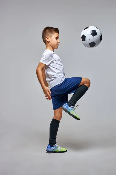 Menino chutando bola de futebol por joelho isolado em cinza — Fotografia de Stock