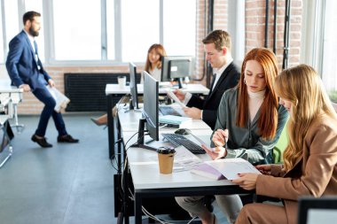 Modern ofiste oturan ve bilgisayar kullanan genç iş kadınları,