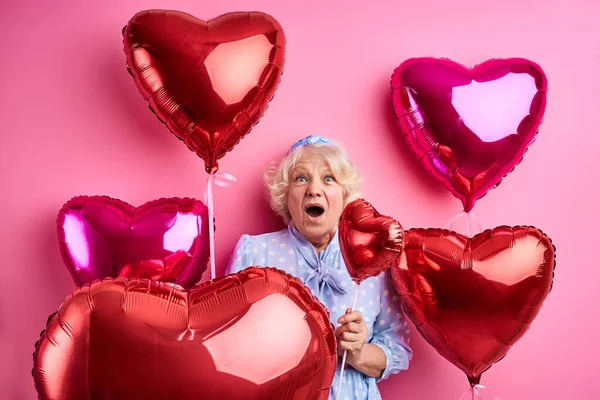 senior surprised lady has party having red air balloons, wears fashionable clothes