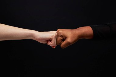 Karma ırk çeşitliliğine sahip insanların siyah arka planda yumruk tokuşturması.