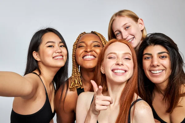 portrait of cheerful diverse women taking selfie, looking at camera