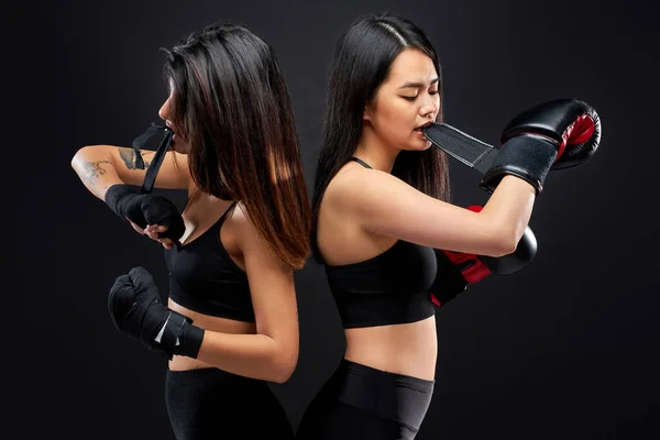 Two sportive women tying bandage for boxing with mouth, teeth — Stock Photo, Image