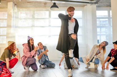 Bir grup genç, hafif stüdyo arka planında şık kıyafetler içinde hip-hop yapıyor.