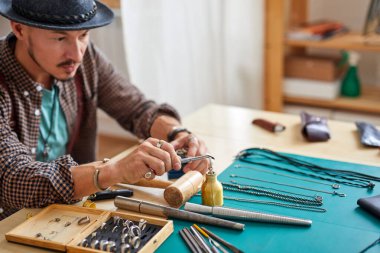 Deneyimli genç kuyumcu bir atölyede el yapımı bir mücevher üzerinde çalışıyor.