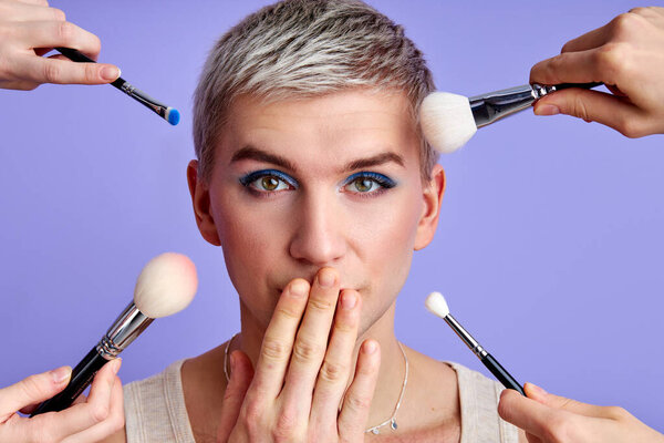 шокированный женственный мужчина и кисти для макияжа