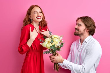 Pastel pembe arka planda izole edilmiş parti kıyafetli heyecanlı genç çift, Sevgililer Günü