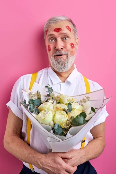 mature caucasian man with lipstick marks on face holding flowers as gift, stand in shock