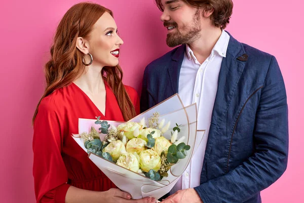 Cheerful young couple in party clothing standing isolated over pink background, celebrating — Stock Photo, Image