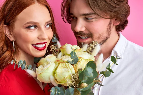 Kärleksfull kaukasisk man som erbjuder sin partner rosor på rosa bakgrund — Stockfoto